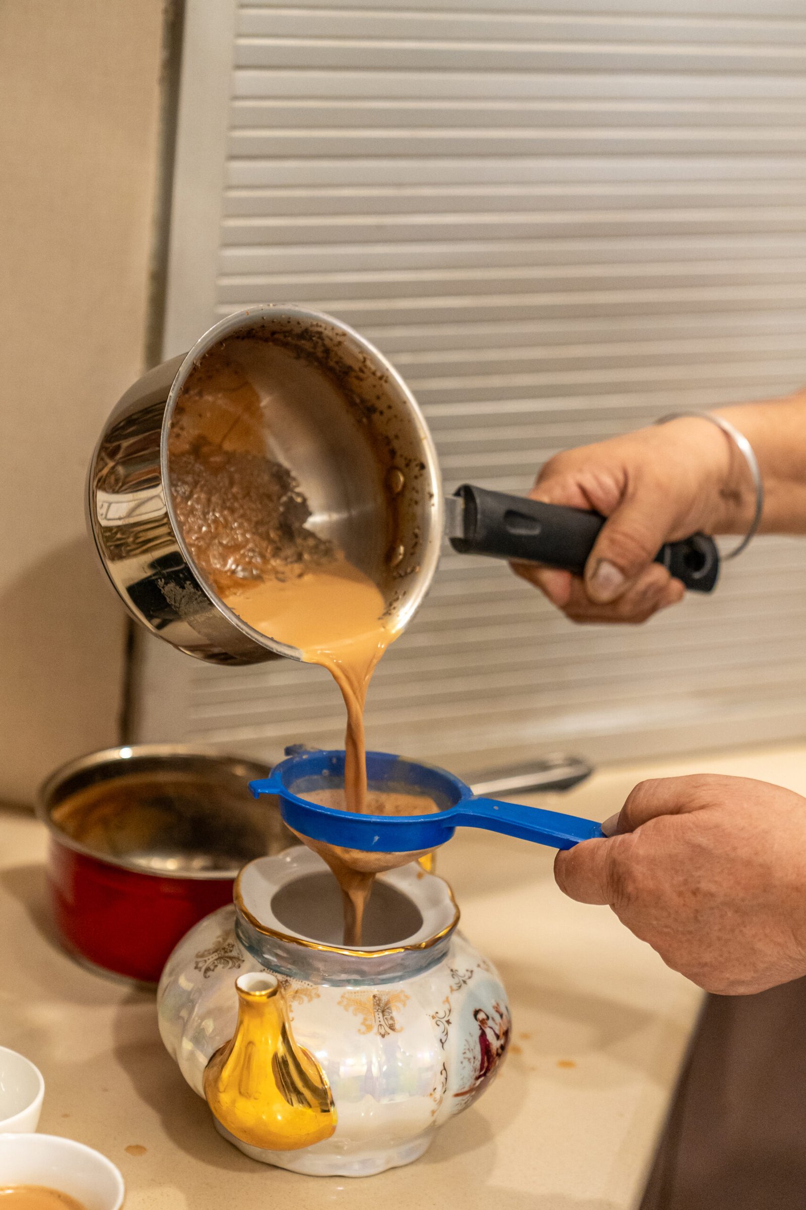 Indian chai being poured through a strainer into cups