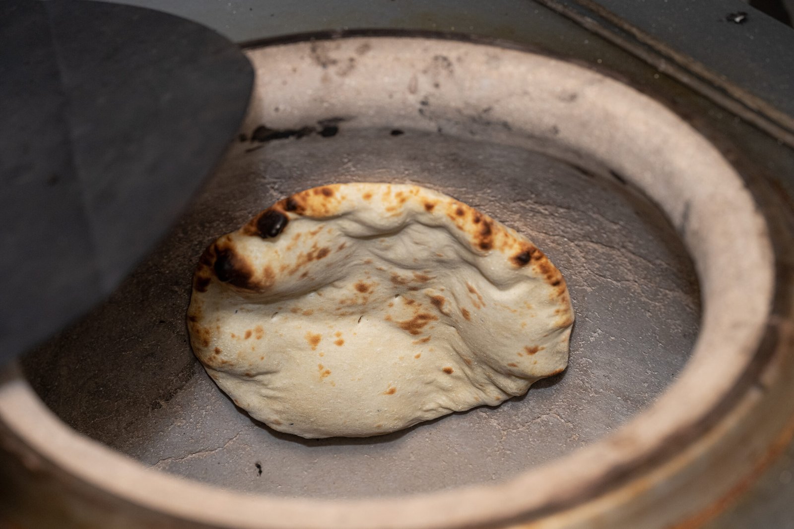 Fresh naan bread baking inside a traditional clay tandoor oven