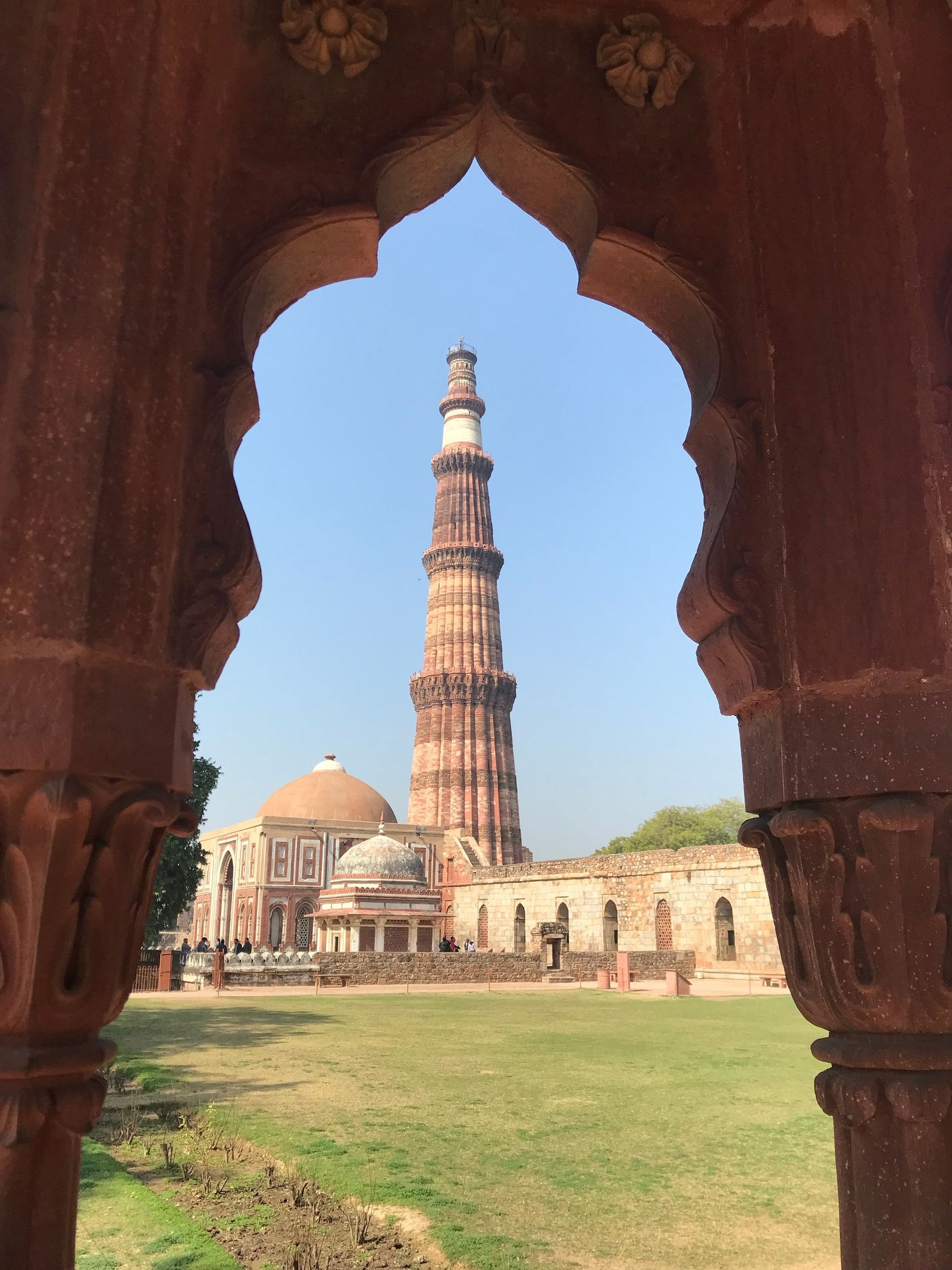 Qutub Minar tower framed through an ancient stone archway in the complex
